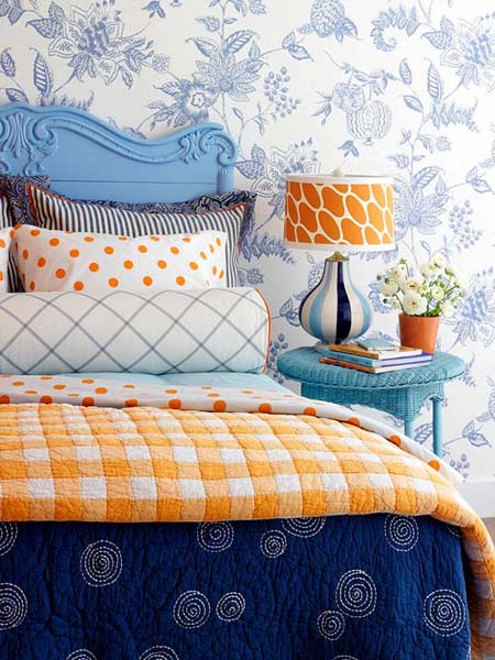 blue wallpaper pattern, blue bed headboard and night table with orange table lamp and comforter